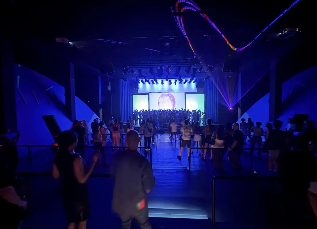 Venue interior lit blue with an audience on the floor